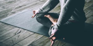 Person der sidder i skrædderstilling på en yogamåtte med hænderne i en rolig position