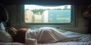 Person der sover under et dyne i en togkupé med godsvogne synlige gennem vinduet