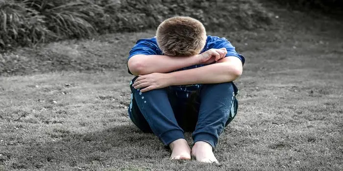 Sort-hvidt billede af en dreng, der sidder nedbøjet på en græsplæne med hovedet skjult i armene