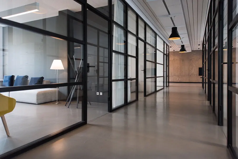 Moderne kontorinteriør med glasvægge, sofa og gulvlampe
