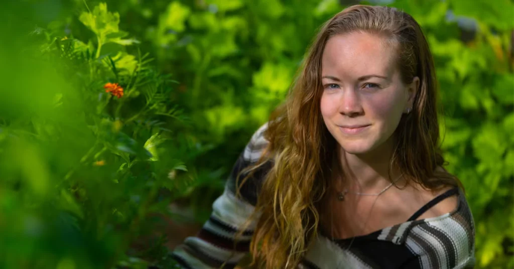 Portræt af en kvinde med langt bølget hår omgivet af grønne planter i en have