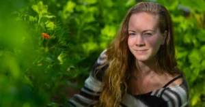 Portræt af en kvinde med langt bølget hår omgivet af grønne planter i en have