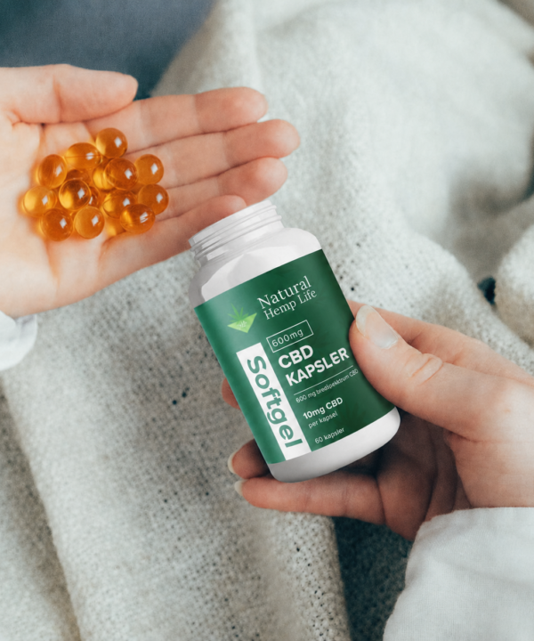 Hånd med gyldne CBD-softgelkapsler (600 mg) ved siden af dåsen fra Natural Hemp Life