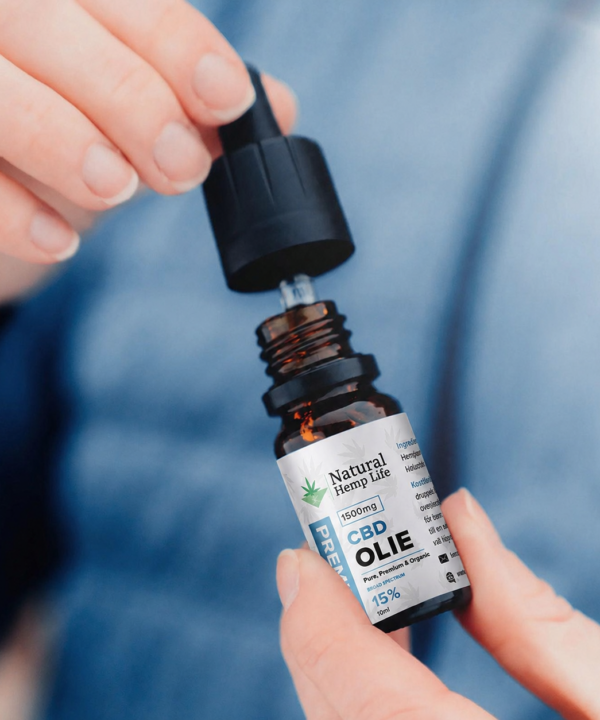 Nærbillede af en hånd, der skruer hætten af en flaske CBD Olie 15% fra Natural Hemp Life, blå baggrund