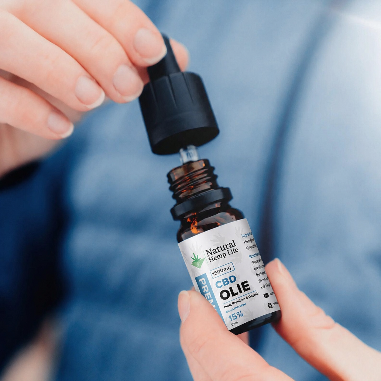 Nærbillede af en hånd, der skruer hætten af en flaske CBD Olie 15% fra Natural Hemp Life, blå baggrund