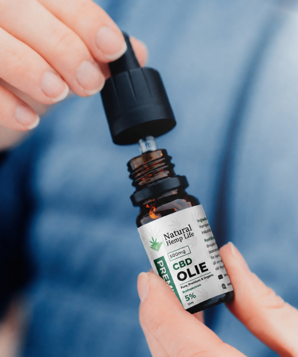 Nærbillede af en hånd, der skruer hætten af en flaske CBD Olie 5% fra Natural Hemp Life, blå baggrund
