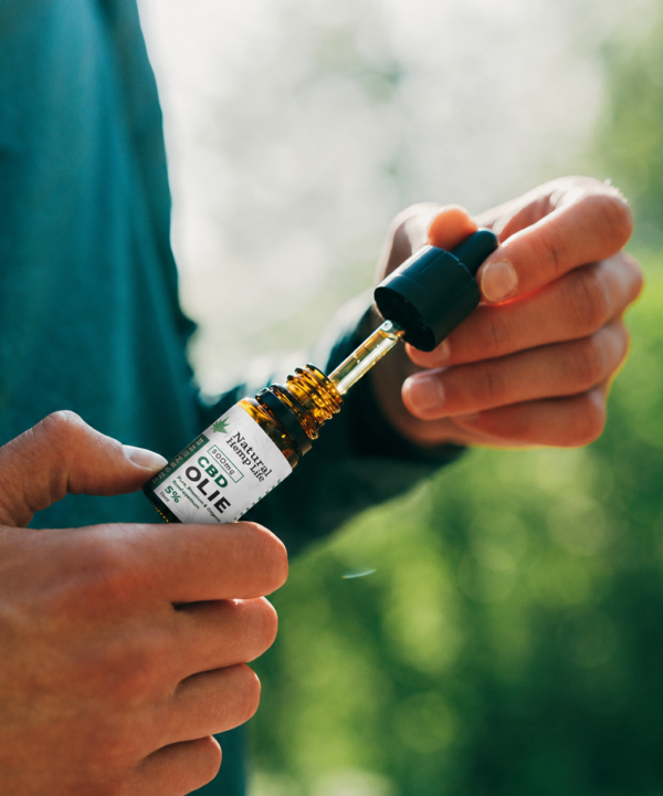 Person i mørkegrøn trøje holder en flaske CBD Olie 5% fra Natural Hemp Life og fylder pipetten